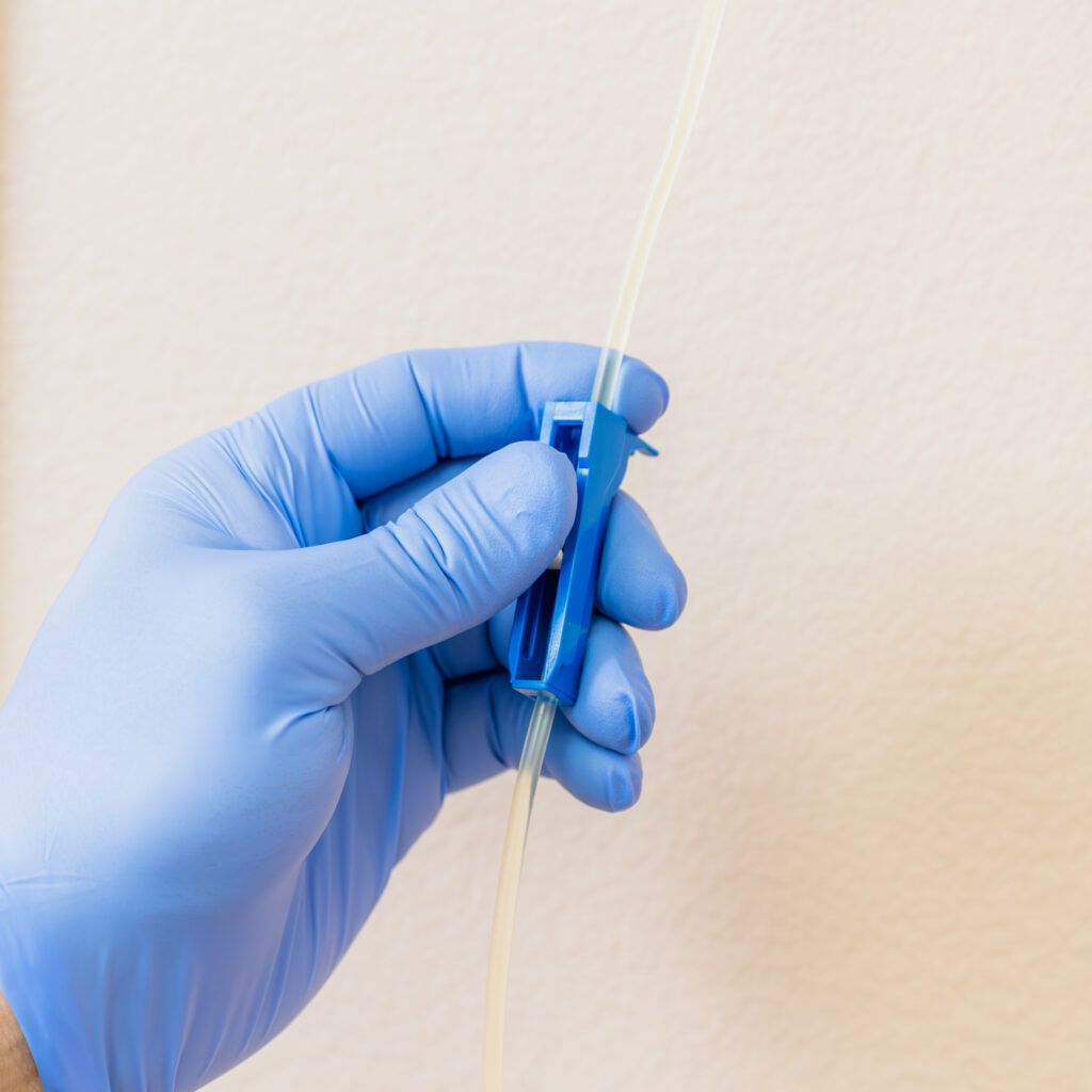 Gloved hand holds plastic tube that carries electrolytes and nutrients from the infusion bag to the person for Hydration IV therapy in Leesburg.