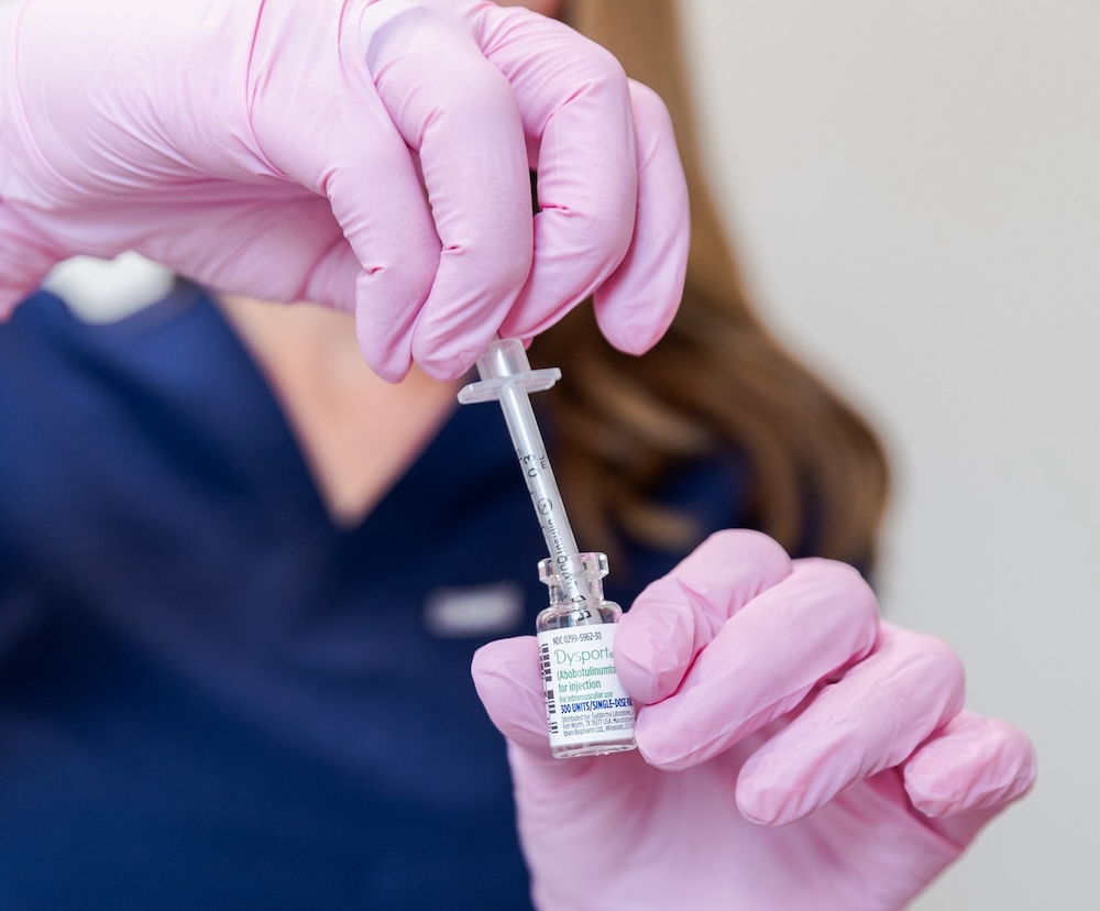 Provider wearing pink gloves holds bottle of Dysport with syringe to treat patient's wrinkles with Botox and fillers near The Villages