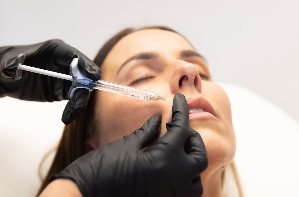 Woman leans head back as provider wearing black gloves injects lip injections near The Villages.