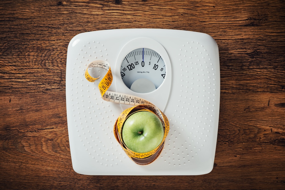 Appe wrapped in measuring tape sitting on top of a scale. This shows some of the tools needed to effectively reach your goals at a weight loss clinic near The Villages.
